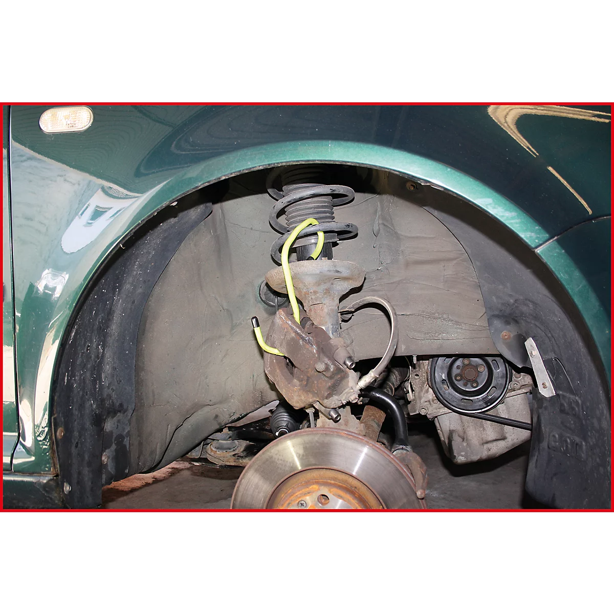 Nahaufnahme des Radkastens eines grünen Autos. Bremsscheibe, Federung, Stoßdämpfer und gelbe Leitungen sind zu sehen.